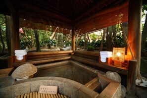A traditional Japanese onsen with stone seating and a bamboo roof structure.
