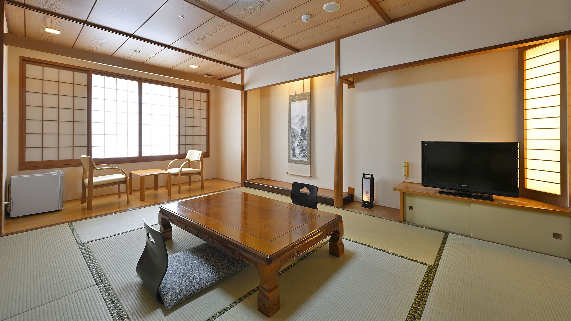 A traditional Japanese-style room with tatami flooring, a low wooden table, a television, and a shoji screen.