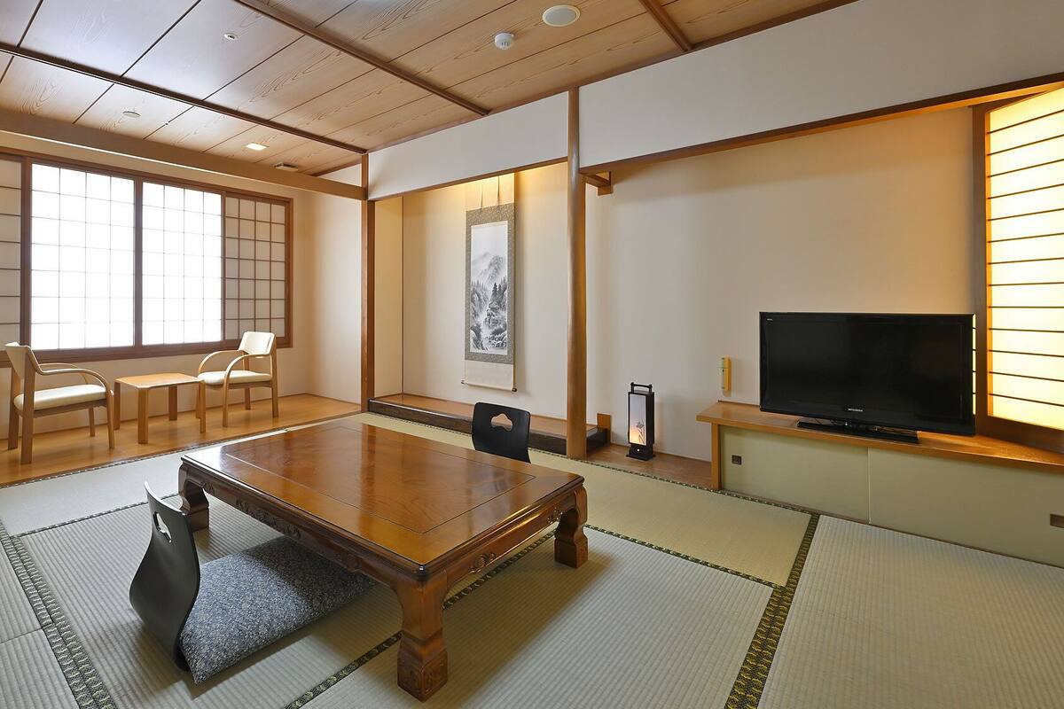 Une pièce de style japonais traditionnel, avec un sol recouvert de tatamis, une petite table en bois, un téléviseur et un paravent en papier de riz (shoji).