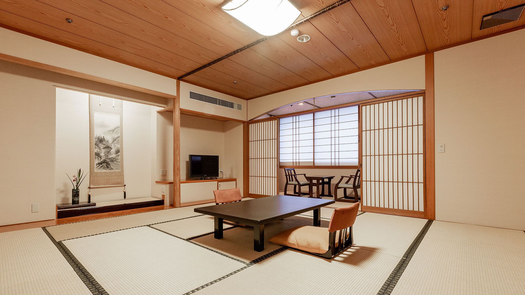Une pièce de style japonais traditionnel, avec un sol recouvert de tatamis, une table basse, des chaises, un téléviseur et des portes coulissantes en papier de riz (shoji).