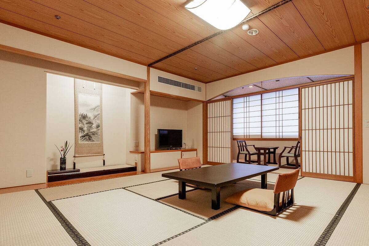 Une pièce de style japonais traditionnel, avec un sol recouvert de tatamis, une table basse, des chaises, un téléviseur et des portes coulissantes en papier de riz (shoji).