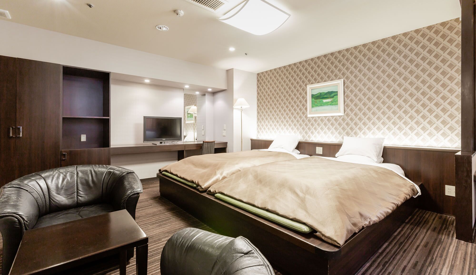 Une chambre d’hôtel avec un lit, deux chaises, un bureau, une télévision et un tableau au mur.