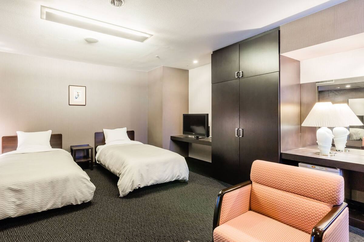 Une chambre d’hôtel avec deux lits, une télévision, une armoire, un bureau avec une lampe et une chaise.