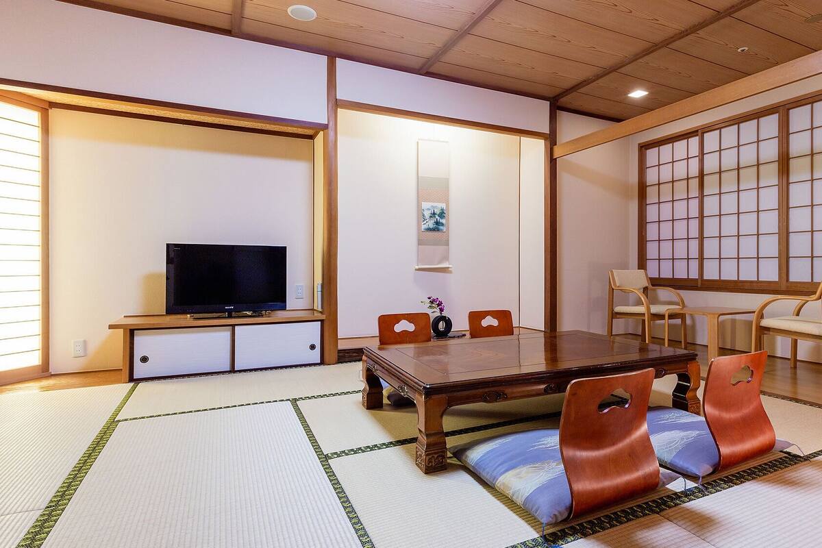 Une pièce de style japonais traditionnel, avec un sol recouvert de tatamis, une table en bois et un téléviseur.