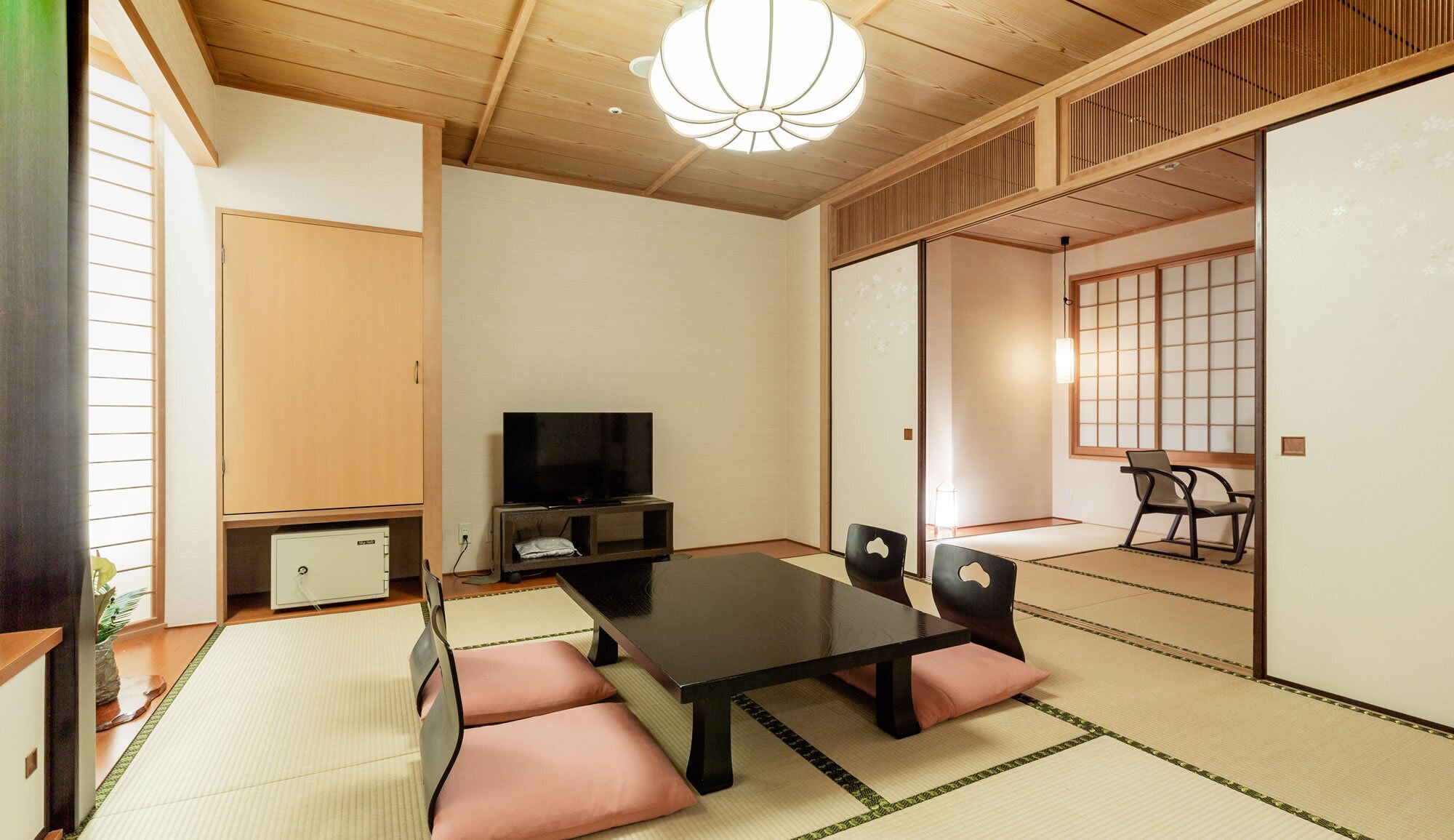 Une pièce de style japonais traditionnel, avec un sol recouvert de tatamis, une table basse avec des coussins, un téléviseur et des portes coulissantes.
