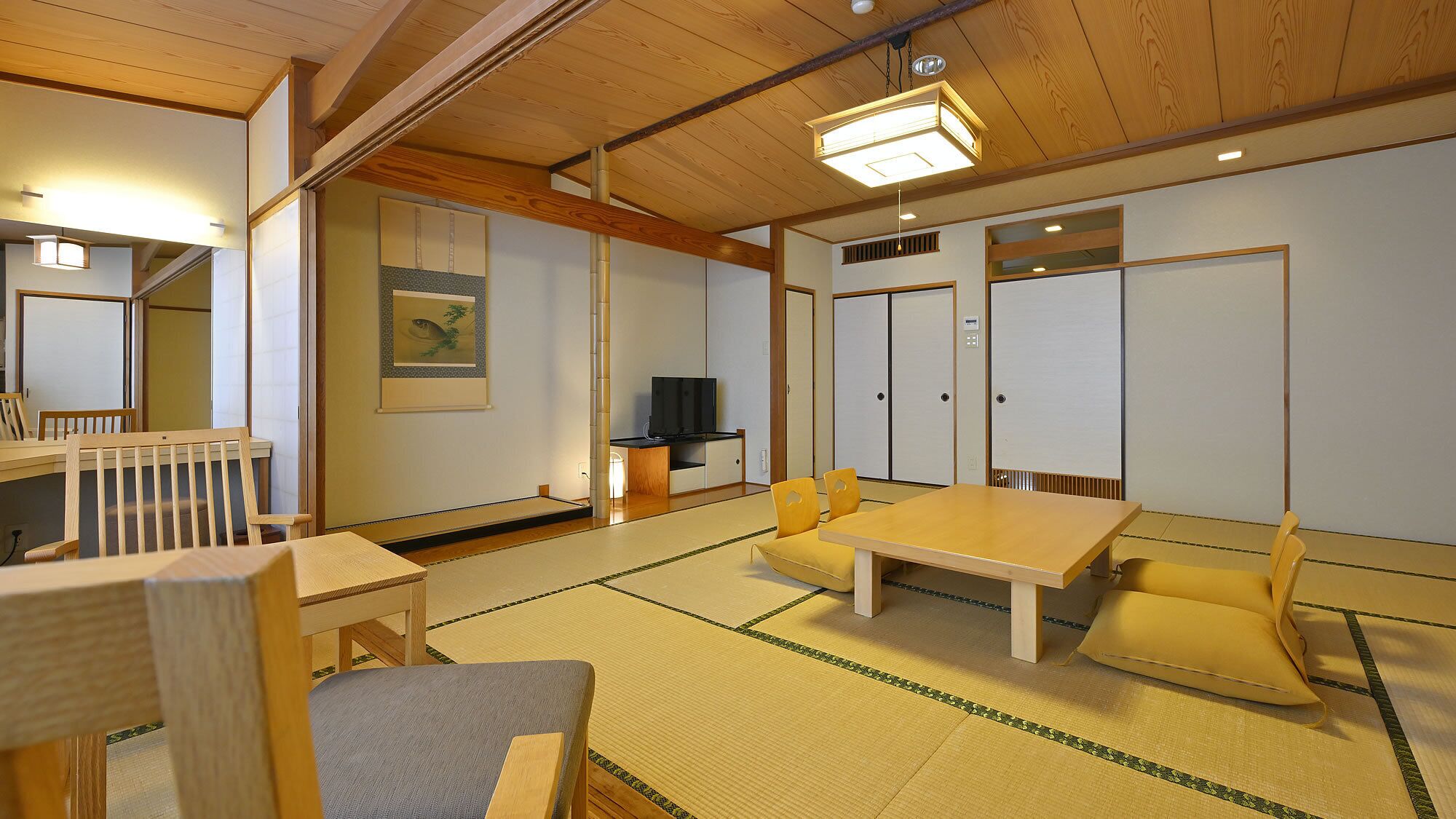 A traditional Japanese room with tatami flooring, a low table, chairs, a television, and sliding doors.
