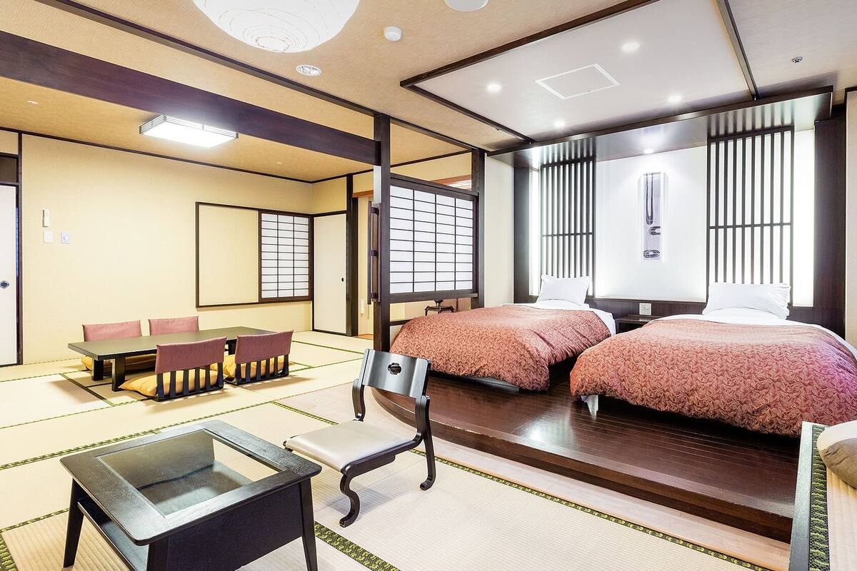 Une pièce de style japonais traditionnel, avec un sol recouvert de tatamis, une table basse, deux lits avec une literie assortie et des paravents en papier de riz (shoji).