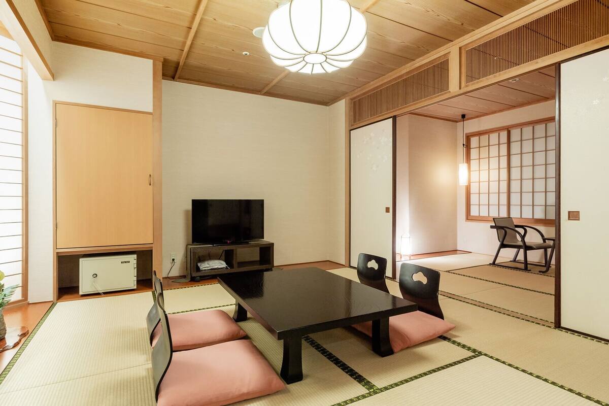Une pièce de style japonais traditionnel, avec un sol recouvert de tatamis, une petite table basse avec des coussins, un téléviseur et des portes coulissantes.