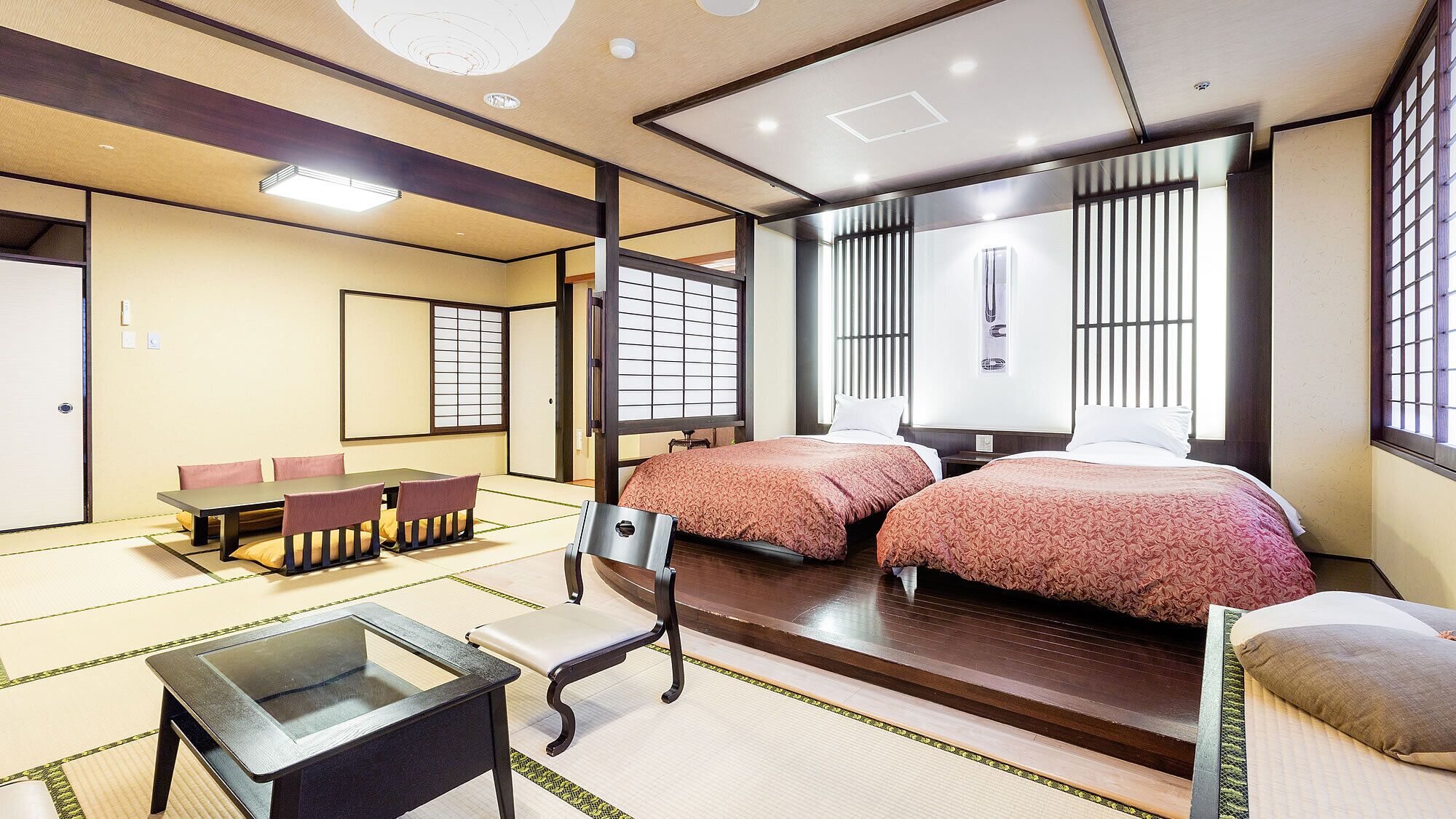 A traditional Japanese-style room with tatami flooring, a low table with cushions, and two beds with matching bedding.
