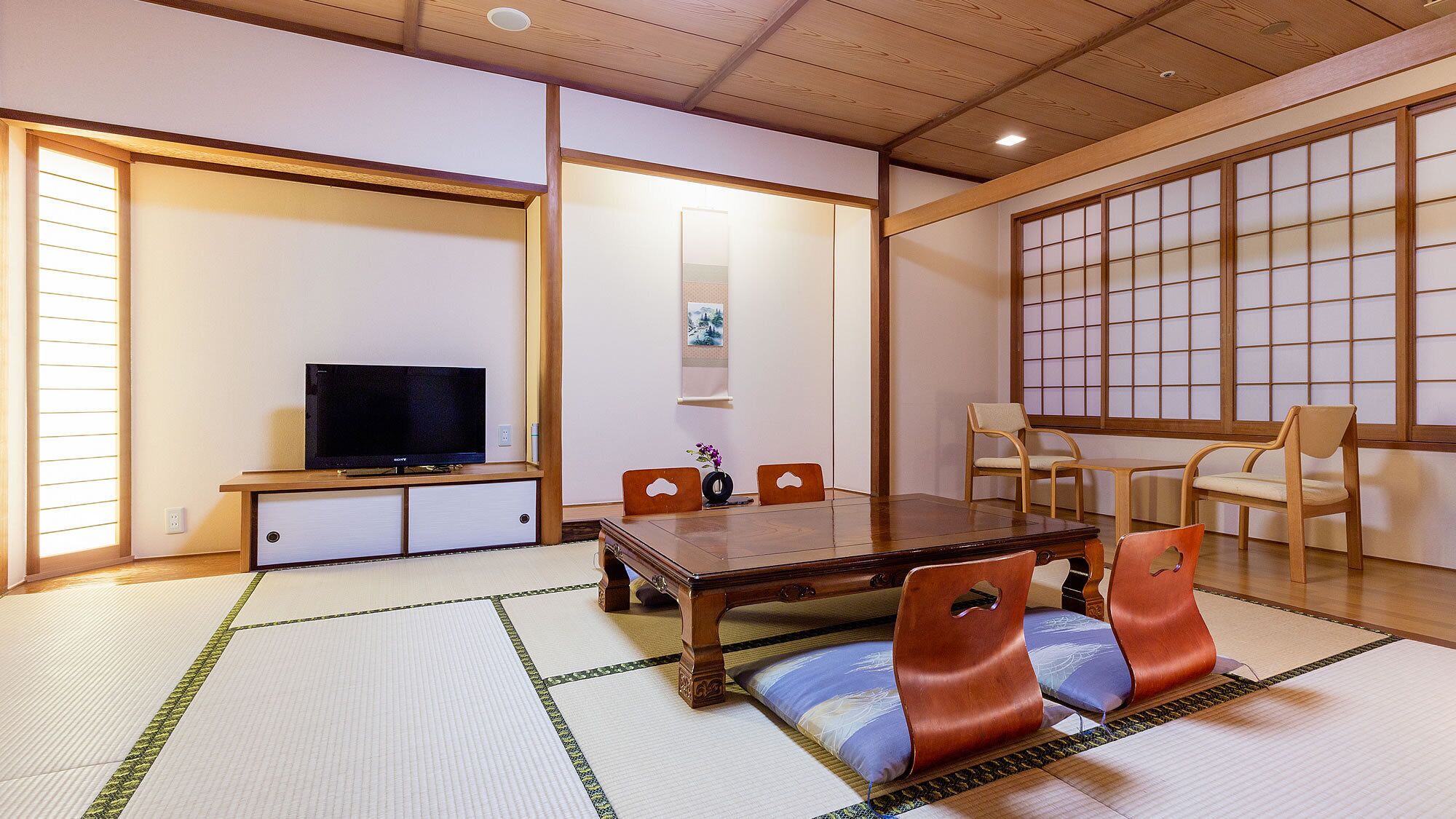 Une pièce de style japonais traditionnel, avec un sol recouvert de tatamis, une télévision, une table en bois et des chaises.