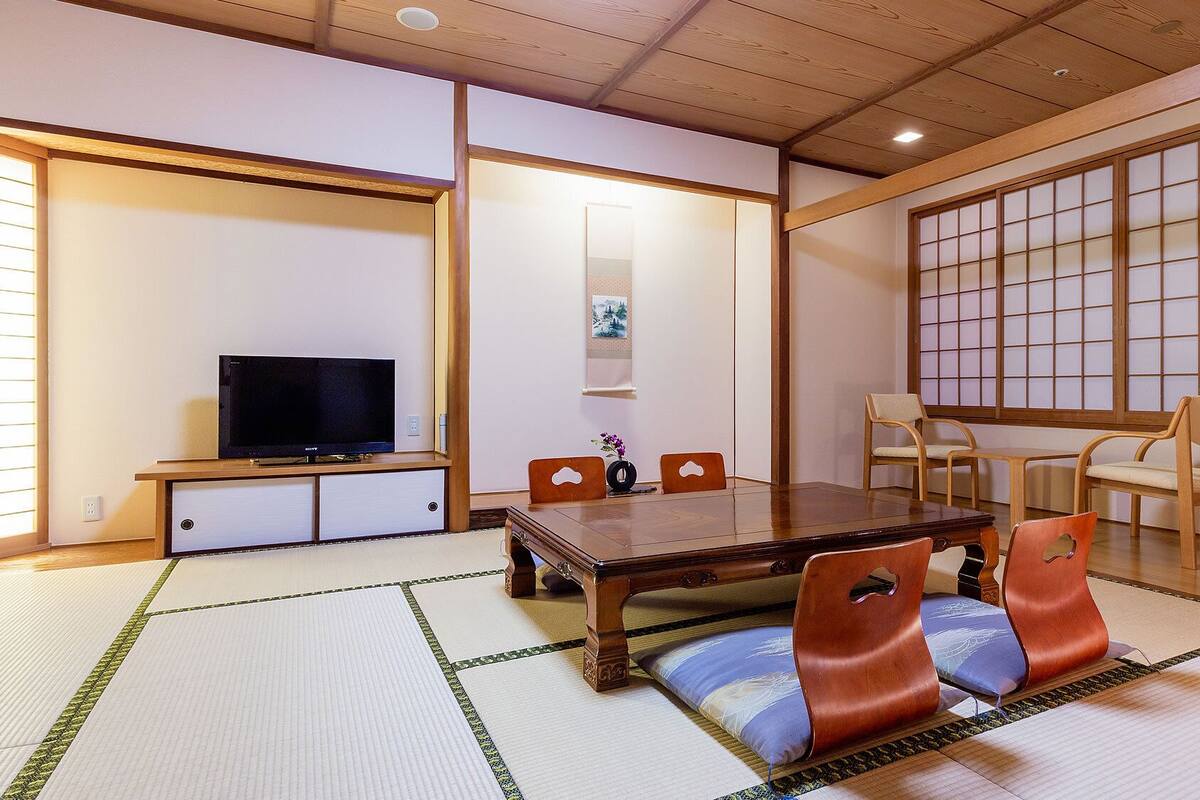 Une pièce de style japonais traditionnel, avec un sol recouvert de tatamis, une télévision, une table en bois et des chaises.