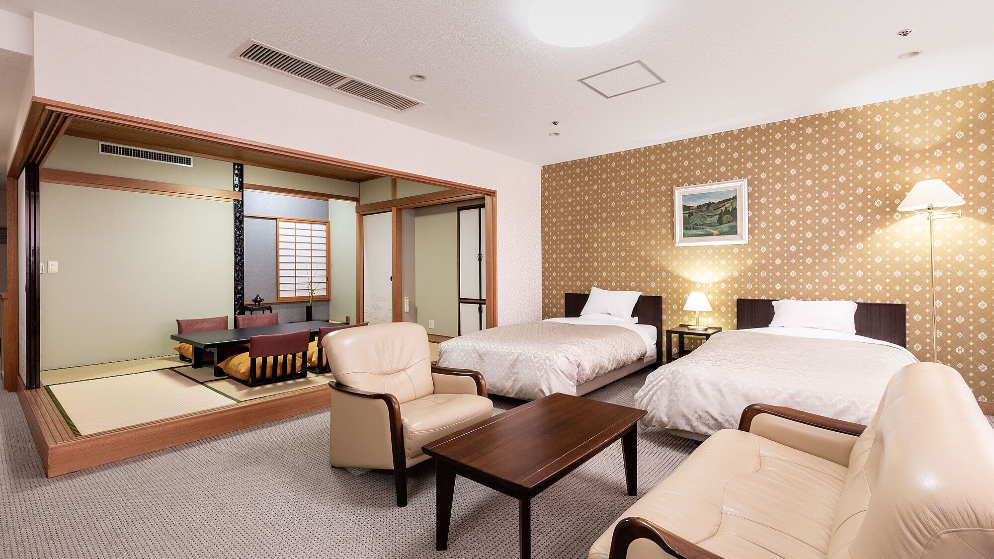 Une chambre d’hôtel comprenant un lit, deux chaises, une petite table, un bureau et une porte coulissante donnant sur un coin repas.