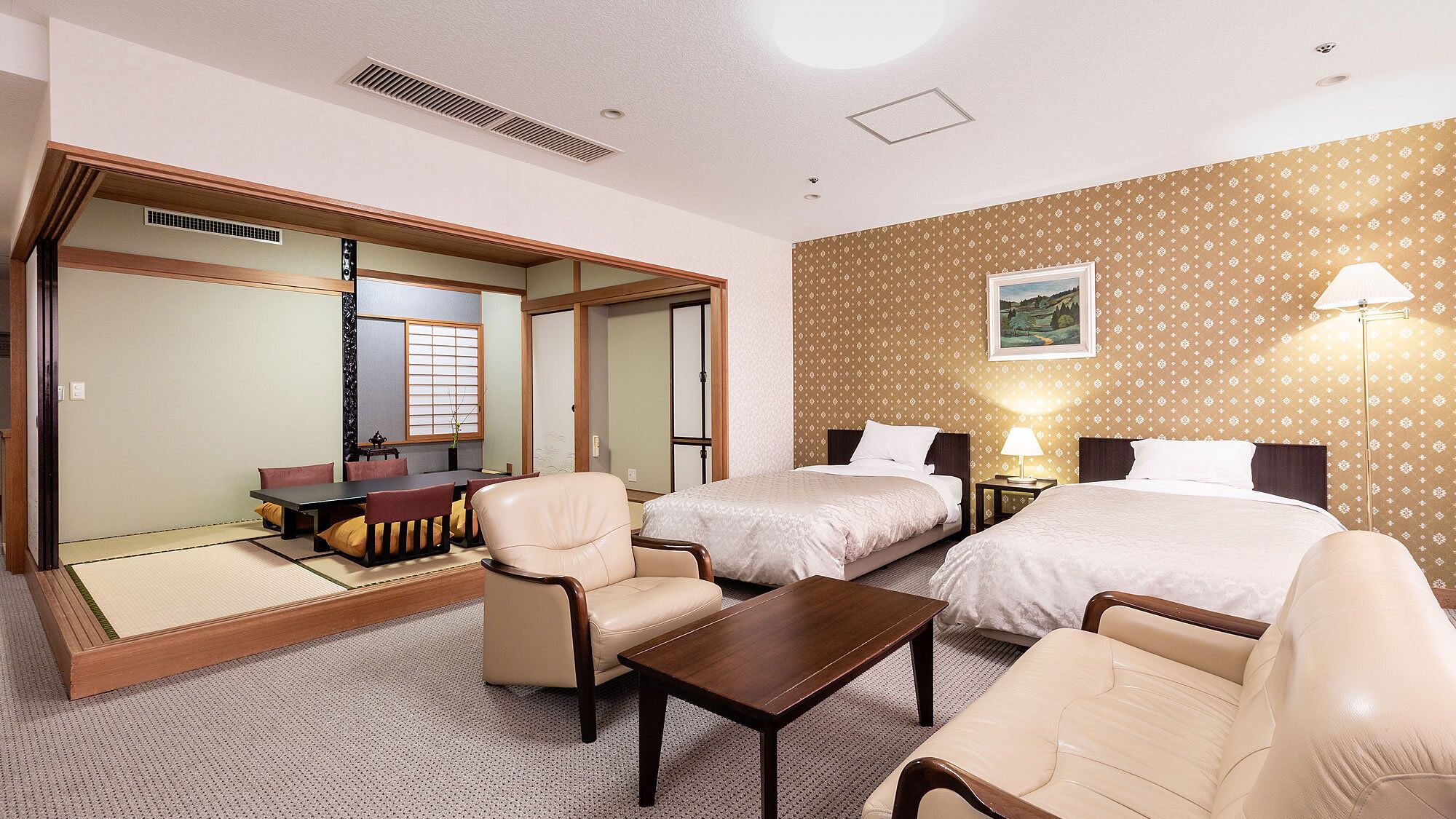 A hotel room with a bed, two chairs, a small table, a desk, a mirror, a picture on the wall, and a window.