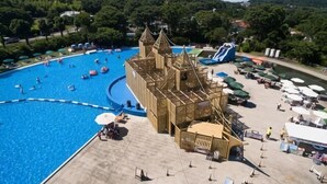 A large swimming pool with a castle-like structure, a water slide, and a sandy area with umbrellas. - Izu One Club (Ito)