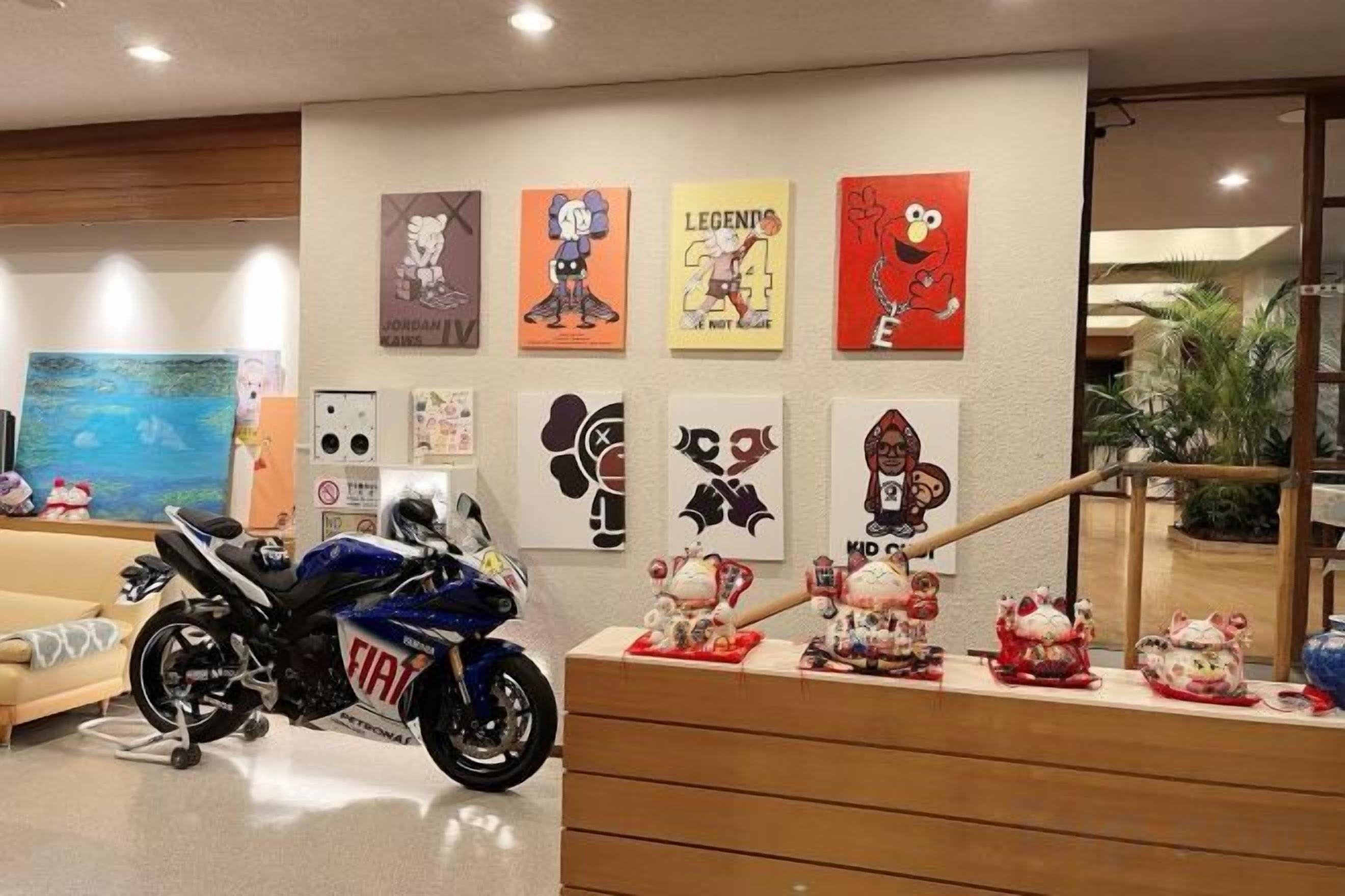Una motocicleta estacionada en una habitación con un muro decorado con varios carteles y una escalera que sube a otro nivel.