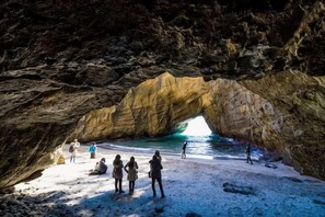 A natural rock arch formation with a beach in front. - Izu One Club (Ito)