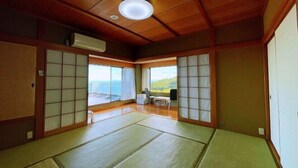 A traditional Japanese room with tatami flooring, sliding doors, and a view of the sea. - Izu One Club (Ito)