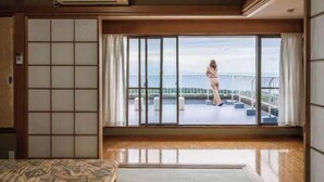 A hotel room with a large sliding glass door leading to a balcony with a view of the sea. - Izu One Club (Ito)