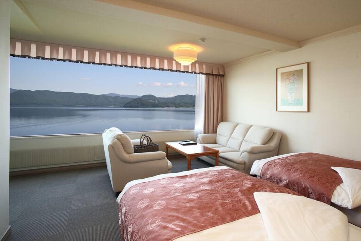 Ein Hotelzimmer mit zwei Betten, einem Sofa, einem Tisch und Blick auf einen See.