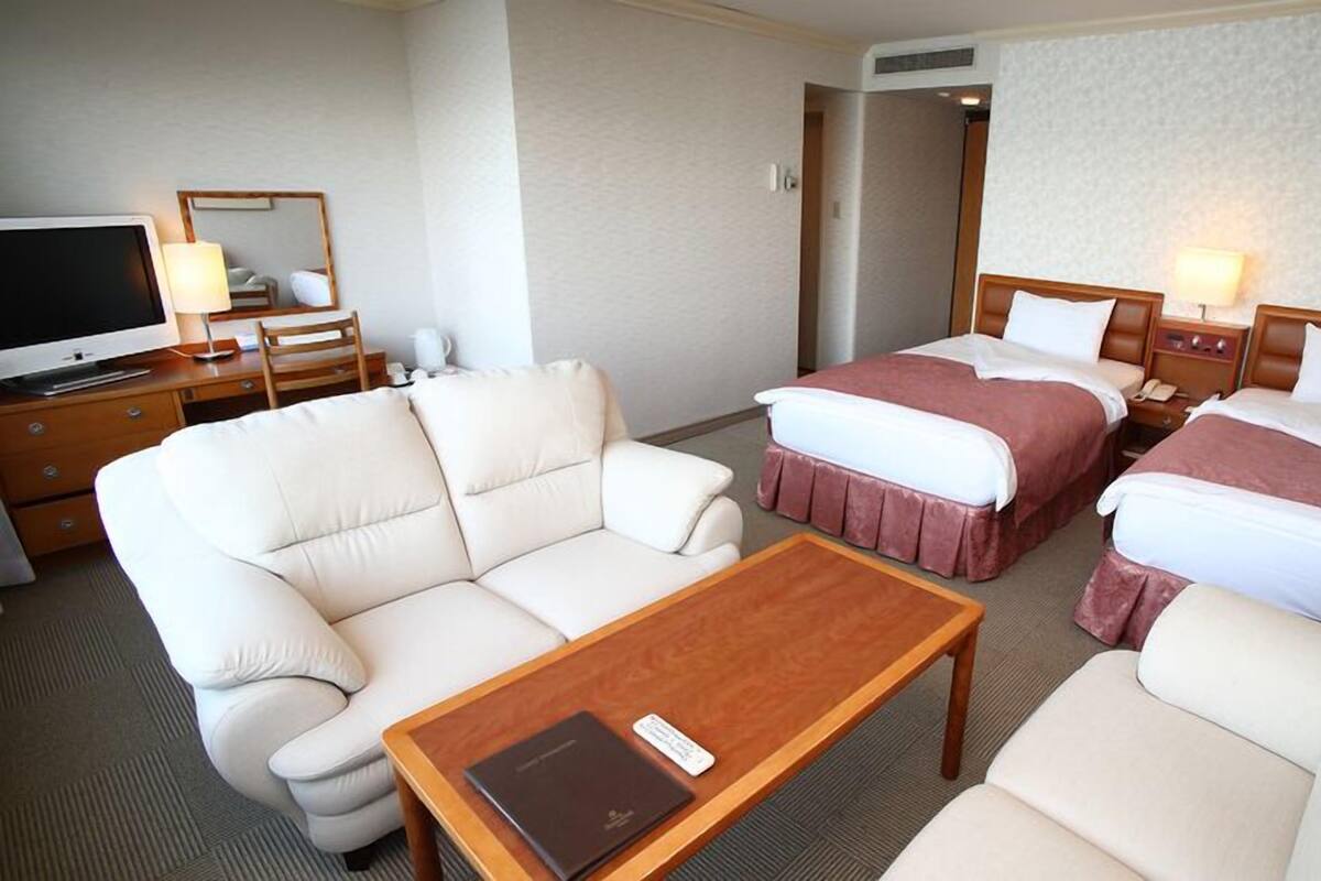 Ein Hotelzimmer mit einer Couch, zwei Betten, einem Fernseher und einem Couchtisch.