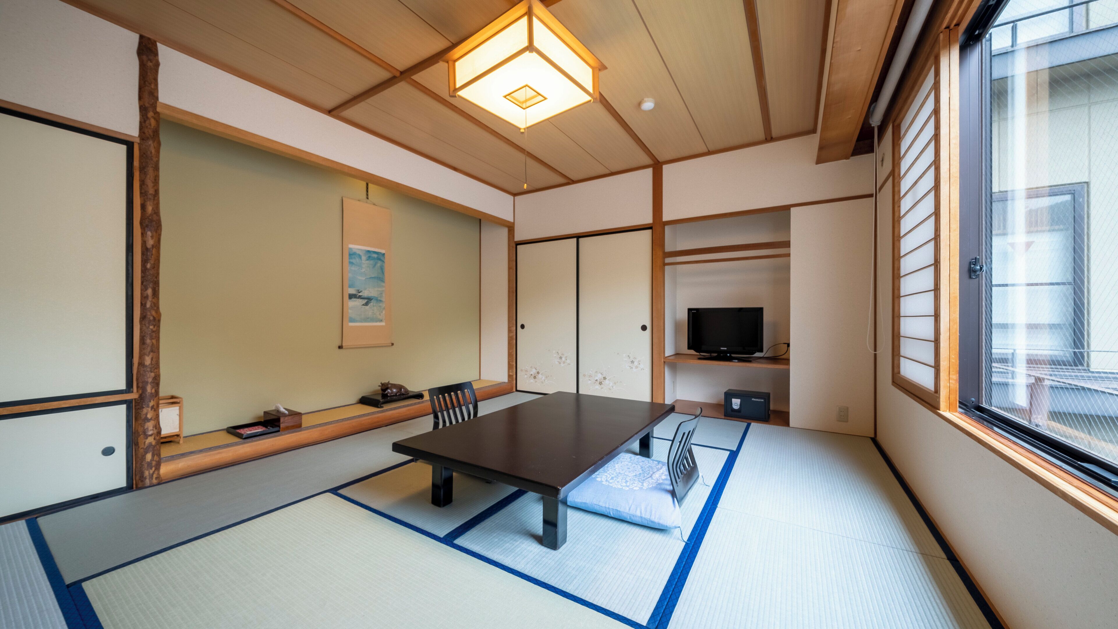 Una habitación tradicional japonesa con suelo de tatami, una mesa baja, un televisor y una puerta corredera.