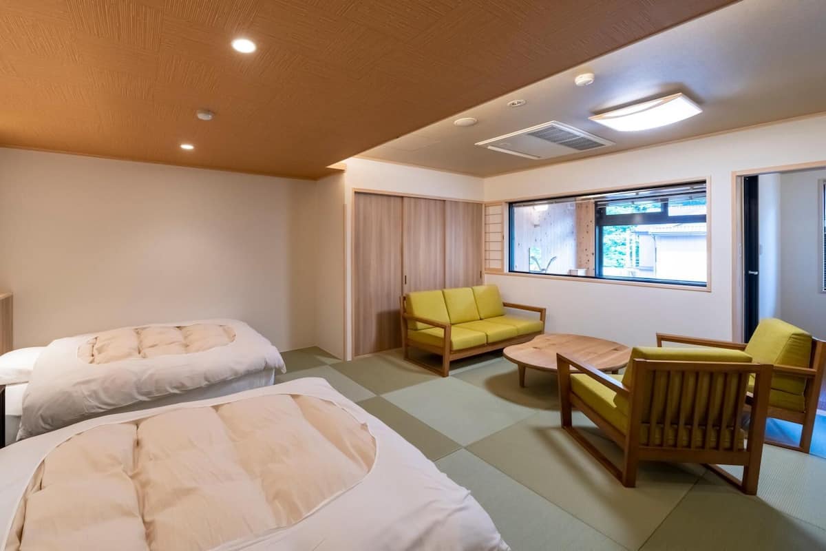 A hotel room with two beds, a sofa, a chair, a small table, and a window with a view.