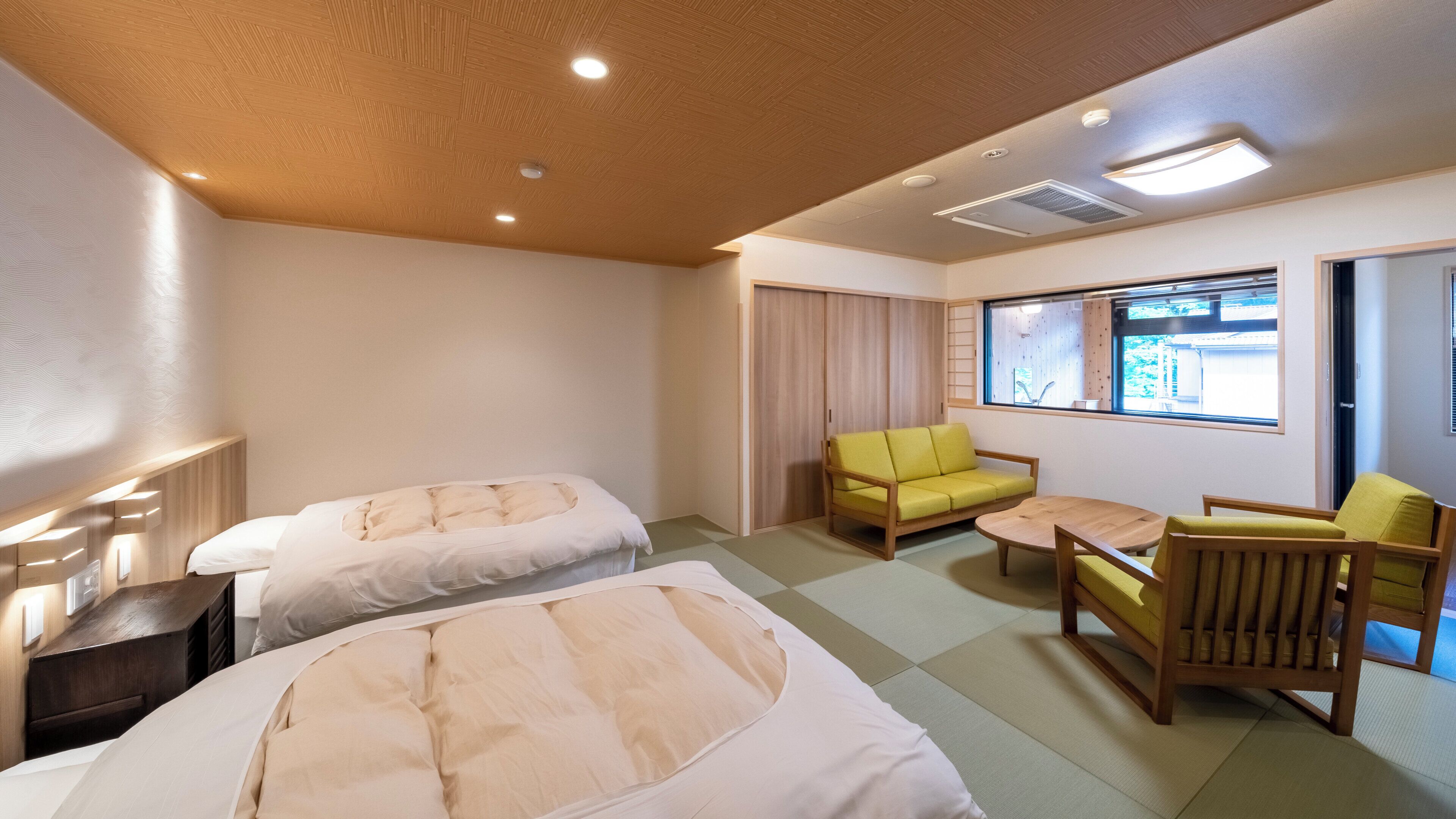 A hotel room with two beds, a sofa, a chair, a small table, and a window with a view.