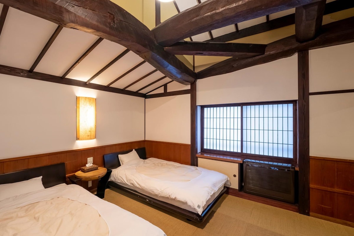 A traditional Japanese-style room with two beds, a wooden ceiling, and a sliding door with a grid pattern.