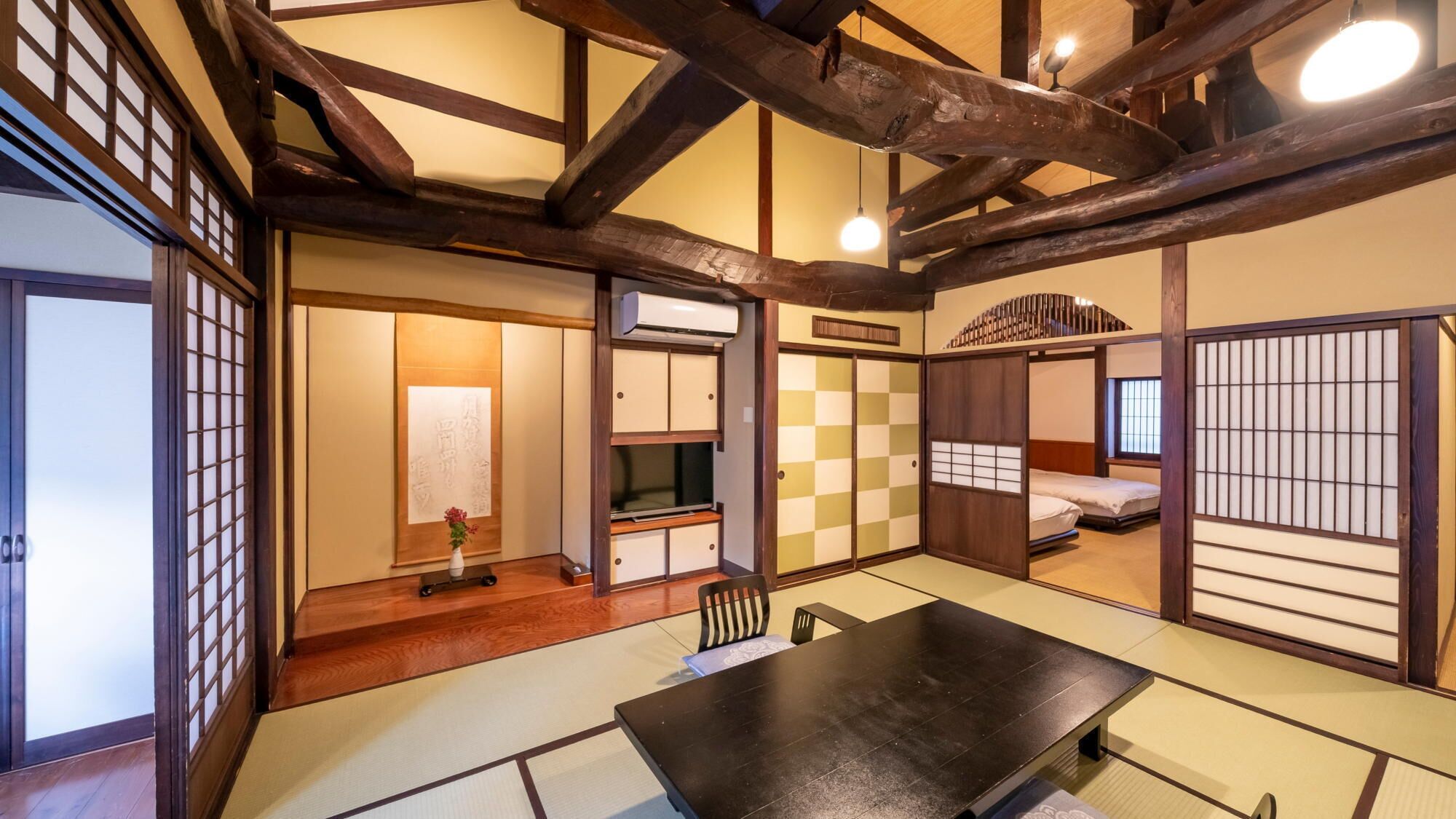 A traditional Japanese room with tatami flooring, a low table, sliding doors, and a bed with a futon.