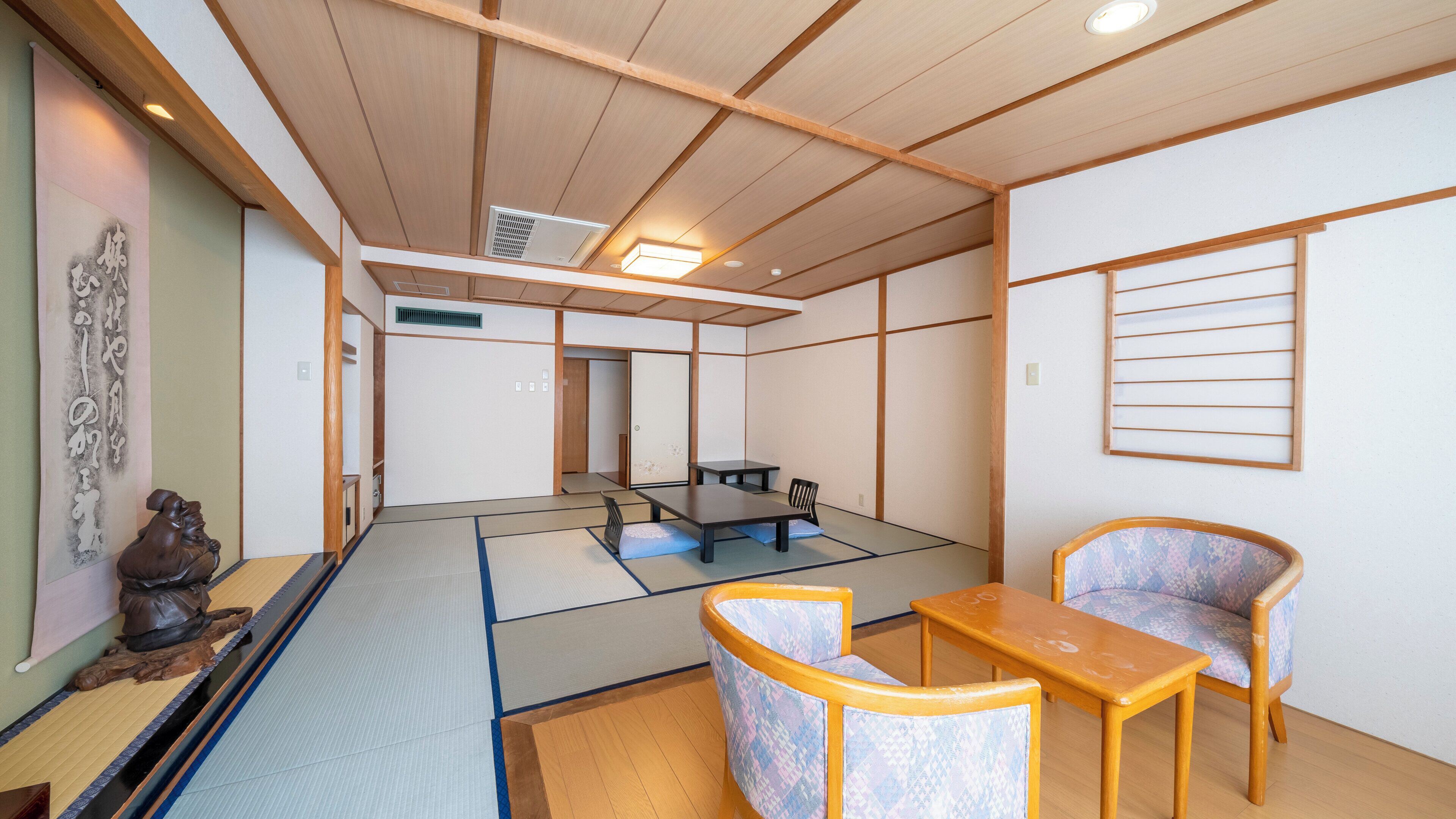 A traditional Japanese room with tatami flooring, a low table, two chairs, a shoji screen, and a hanging scroll.