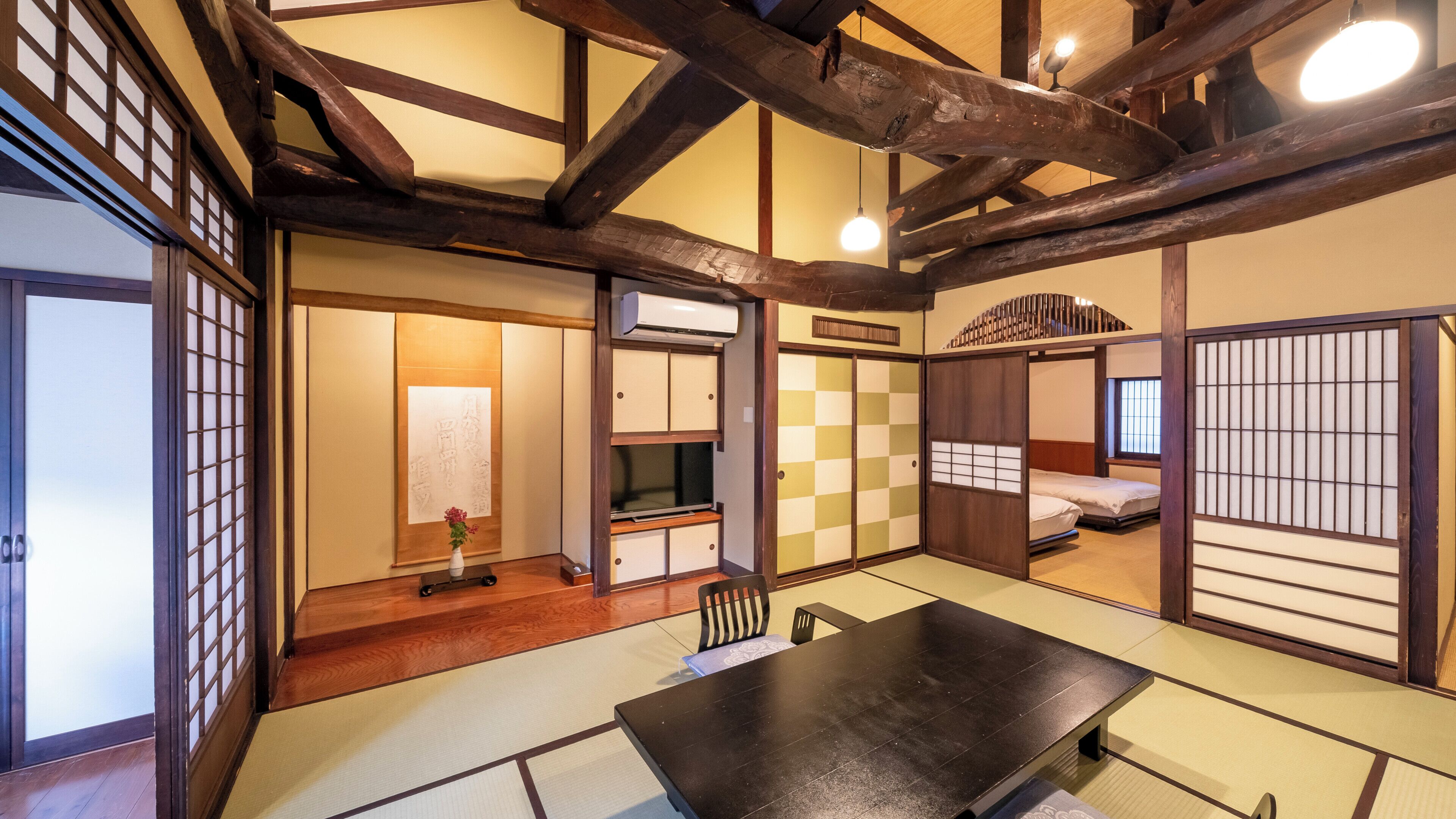 A traditional Japanese room with tatami flooring, a low table, a bed with a shoji screen, and a sliding door.