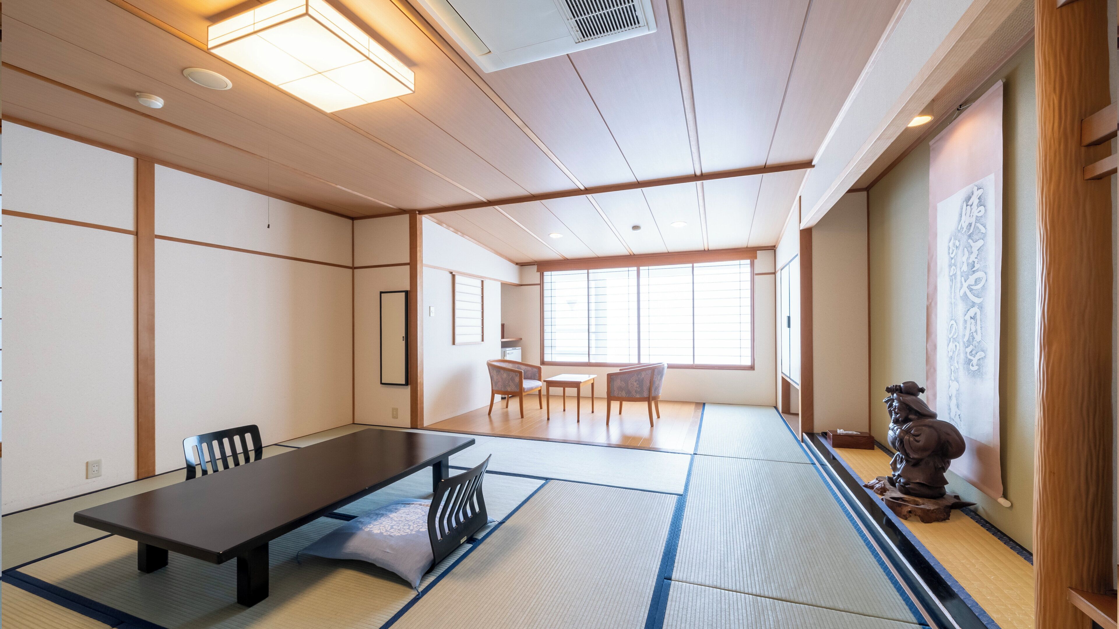 A traditional Japanese-style room with tatami flooring, a low table, chairs, and a sliding door.