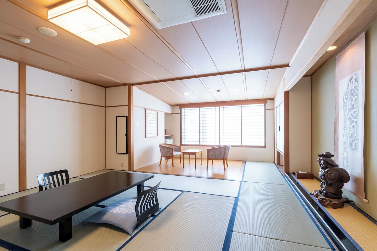 A traditional Japanese-style room with tatami flooring, a low table, chairs, and a sliding door.