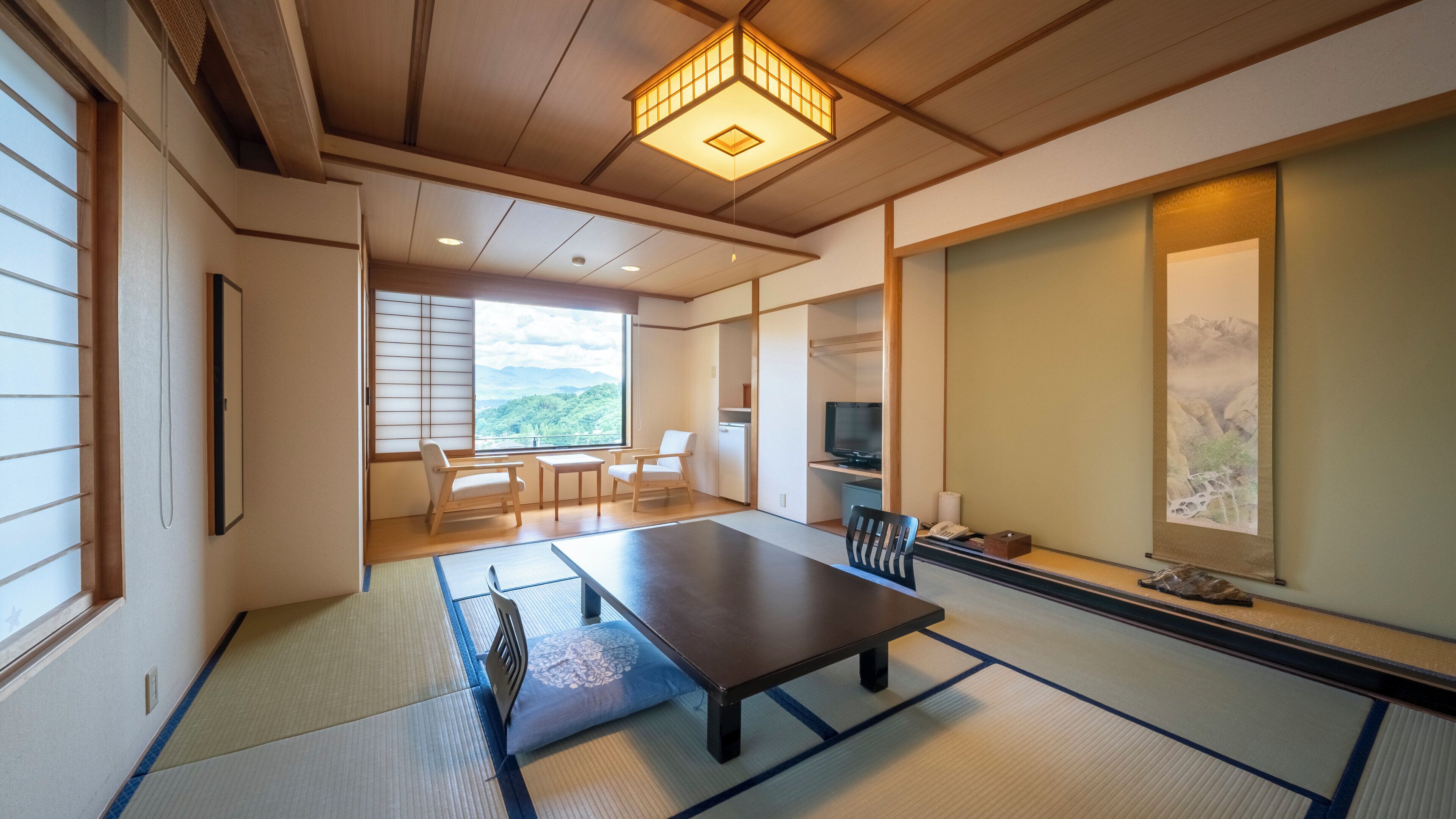 A traditional Japanese room with tatami flooring, a low table, a television, and a view of mountains.