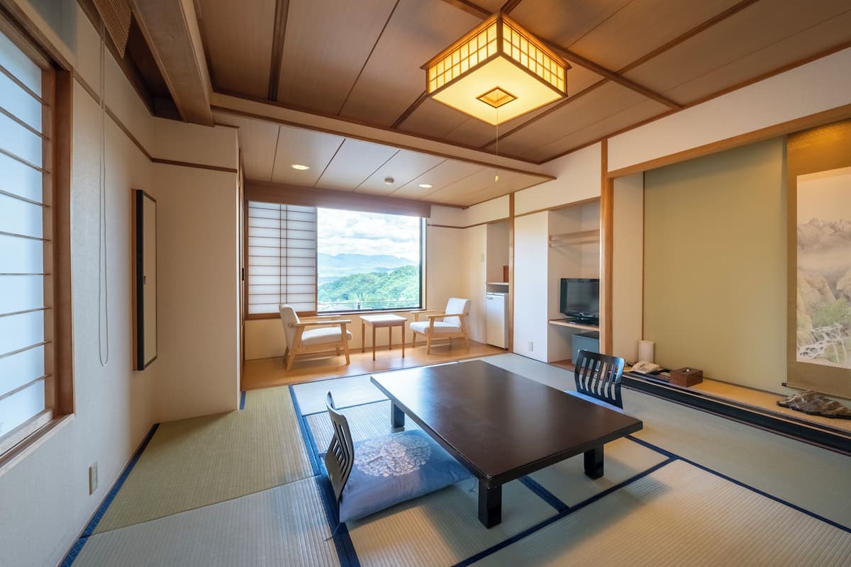 A traditional Japanese room with tatami flooring, a low table, a television, and a view of mountains.