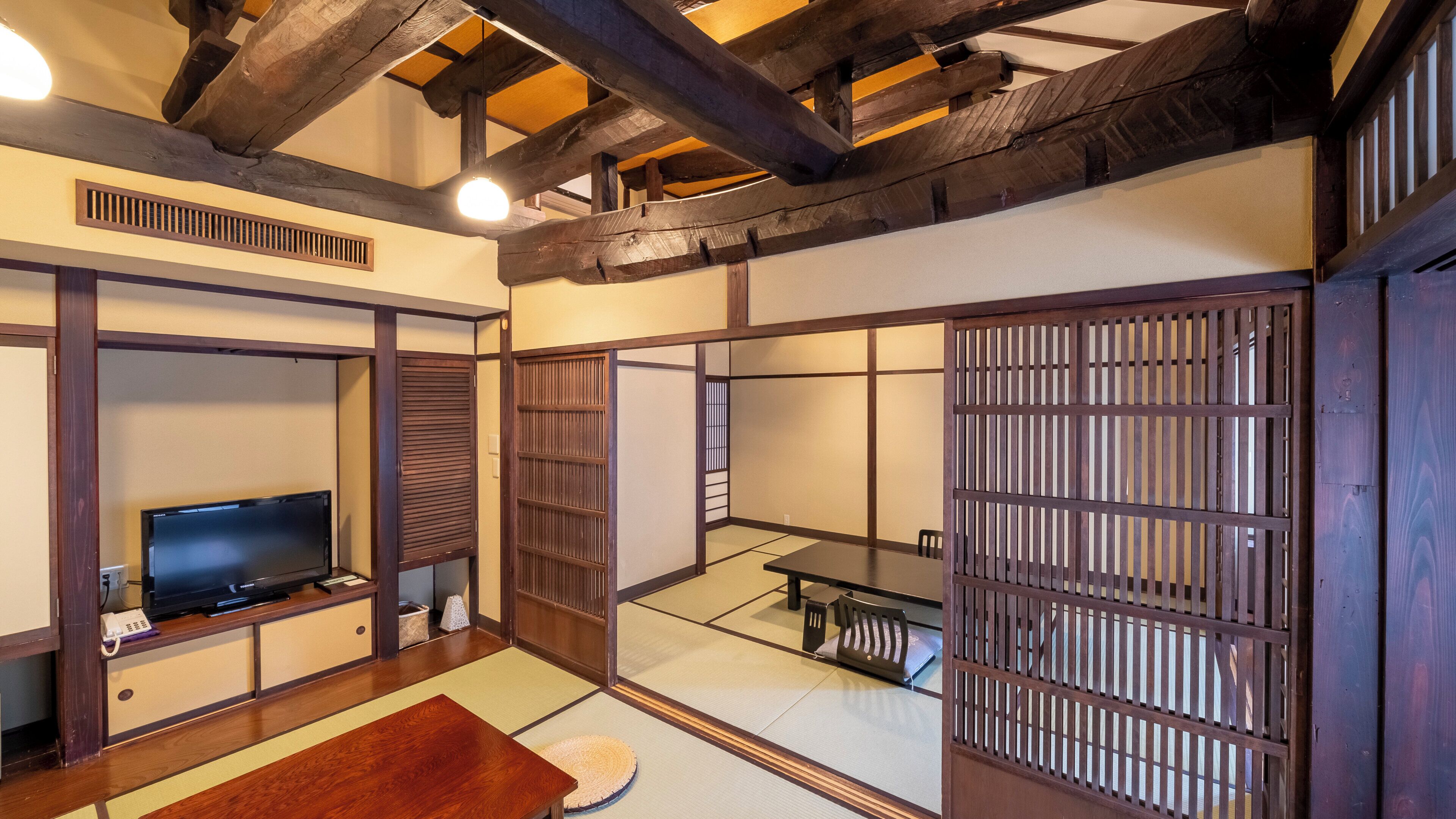 A traditional Japanese room with tatami flooring, a television, a table, and sliding doors.