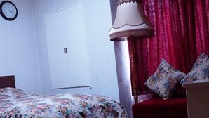 Un dormitorio con una cama, una mesita de noche, una lámpara, un reloj y una cortina roja.
