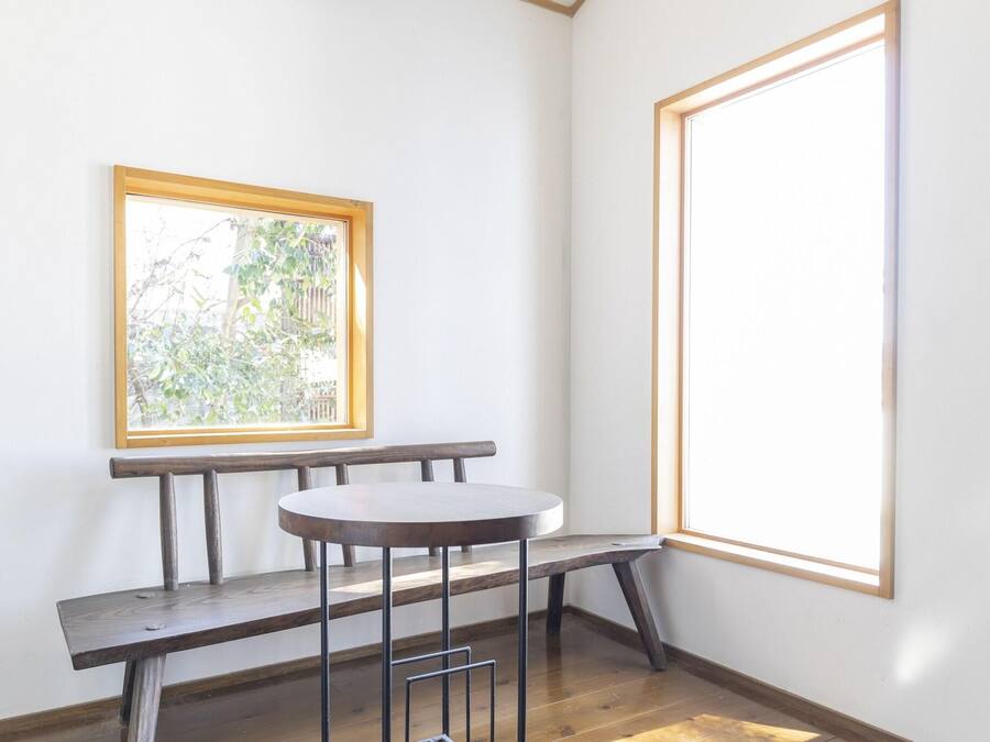 A corner room with a wooden bench, a small round table, and a window with a view of greenery.