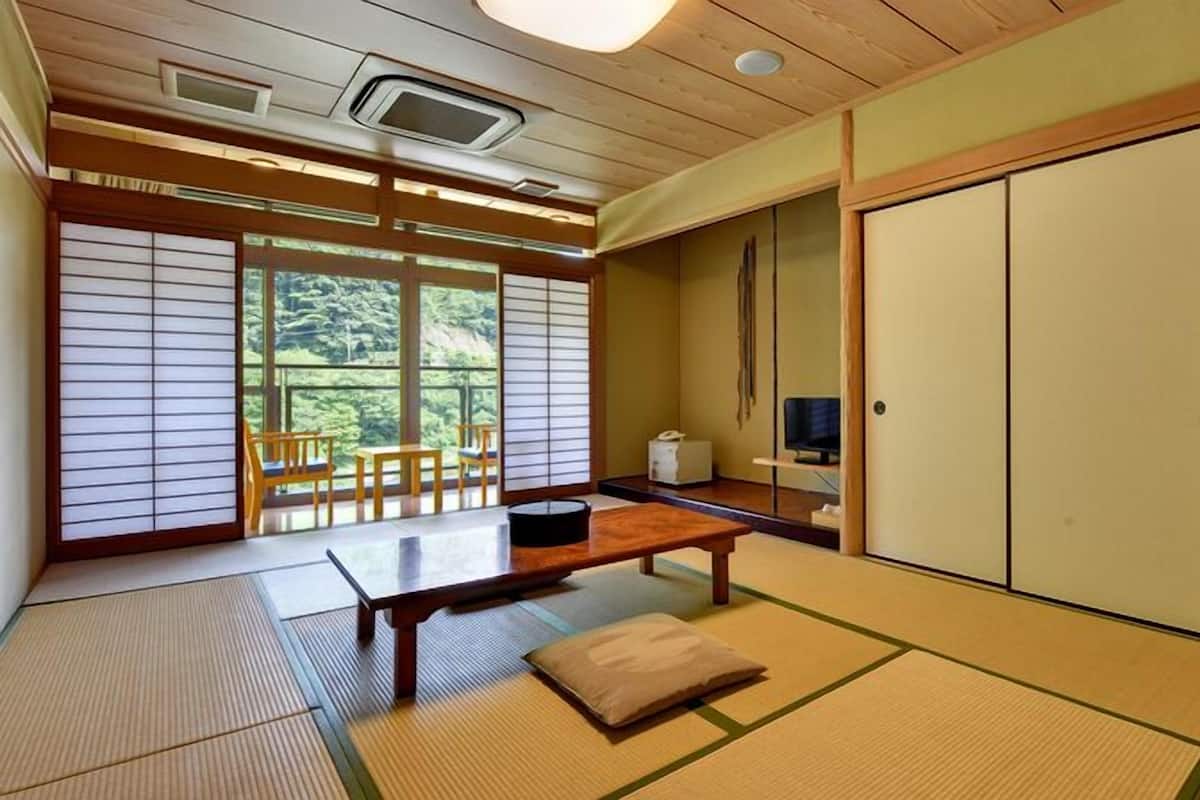 Une pièce de style japonais traditionnel, avec un sol recouvert de tatamis, une table basse, un téléviseur et des portes coulissantes.