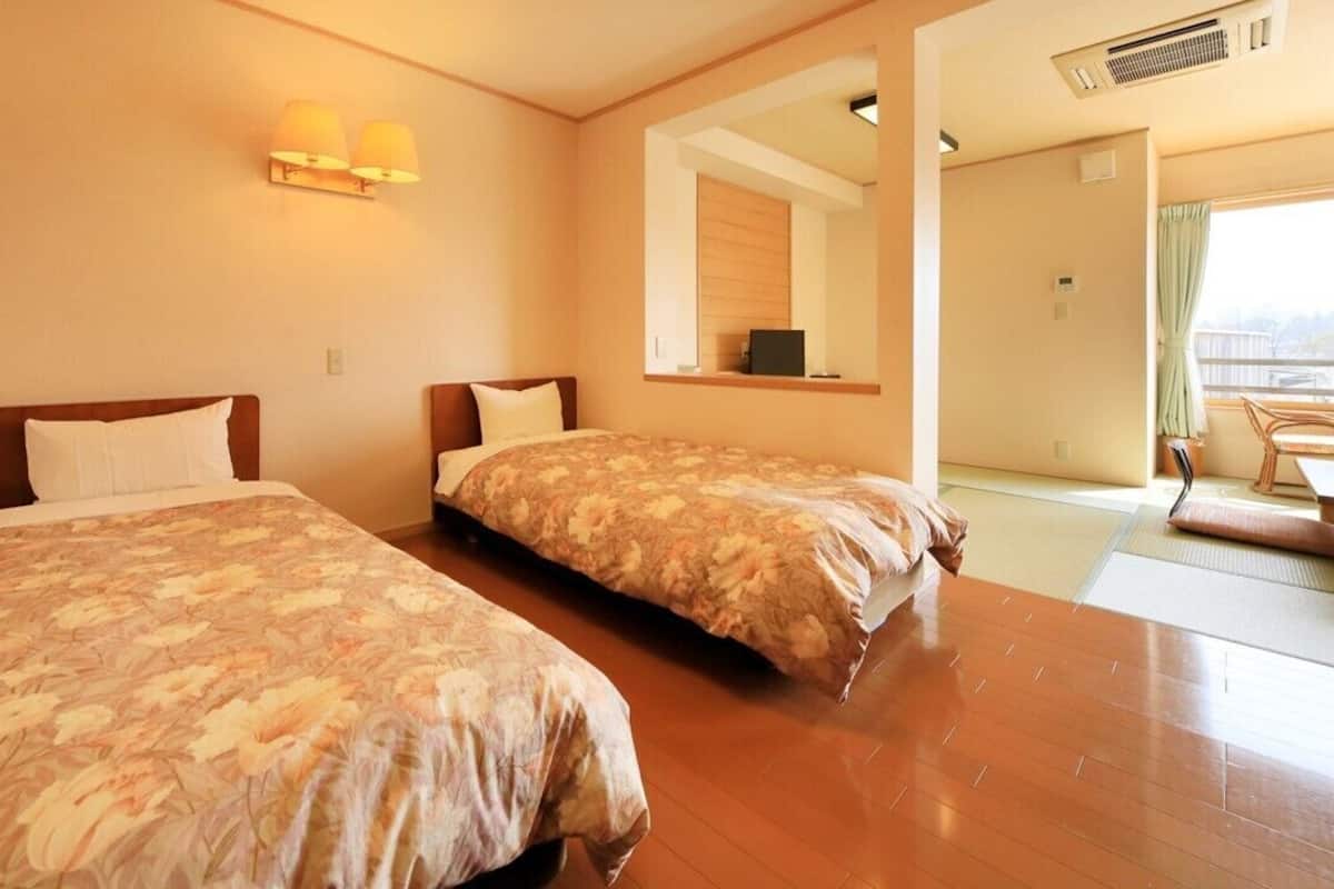 Ein Hotelzimmer mit zwei Betten, einer Sitzecke mit Tisch und Stühlen sowie Blick ins Freie.