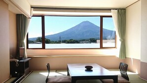 A room with tatami flooring, a low table, a chair, and a view of a mountain. - Fuji Kawaguchiko Onsen Lakeland Hotel Mizunosato (Fujikawaguchiko)
