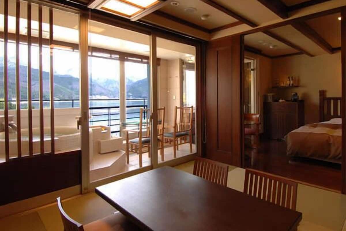 Ein Zimmer mit einer großen Schiebeglaswand, die auf einen Balkon mit Bergblick führt. Im Zimmer befindet sich ein Holztisch und Stühle.