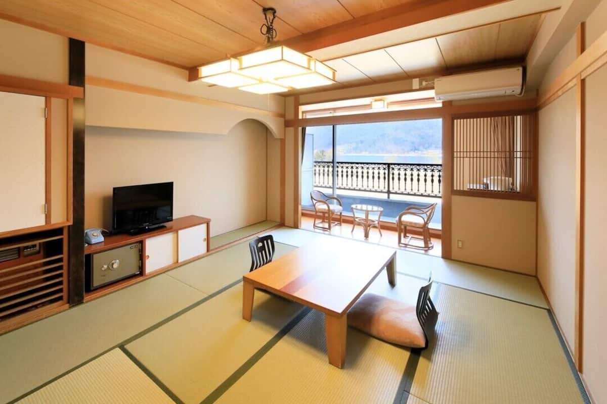 Ein traditioneller japanischer Raum mit Tatami-Boden, einem Fernseher, einem Tisch mit Stühlen und einem Balkon mit Blick.