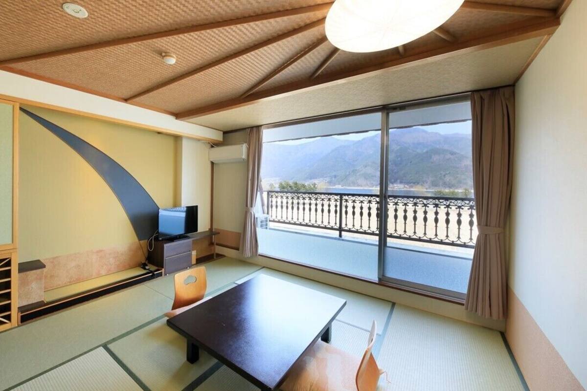 Ein Zimmer mit Tatami-Boden, einer Schiebetür, einem Fernseher und einem Balkon mit Bergblick.