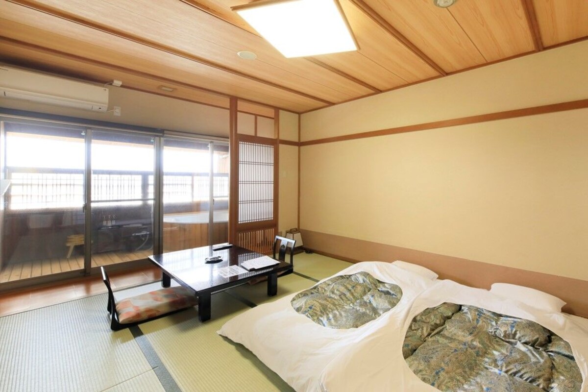 A traditional Japanese room with tatami flooring, a futon bed, a sliding door, and a table with chairs.