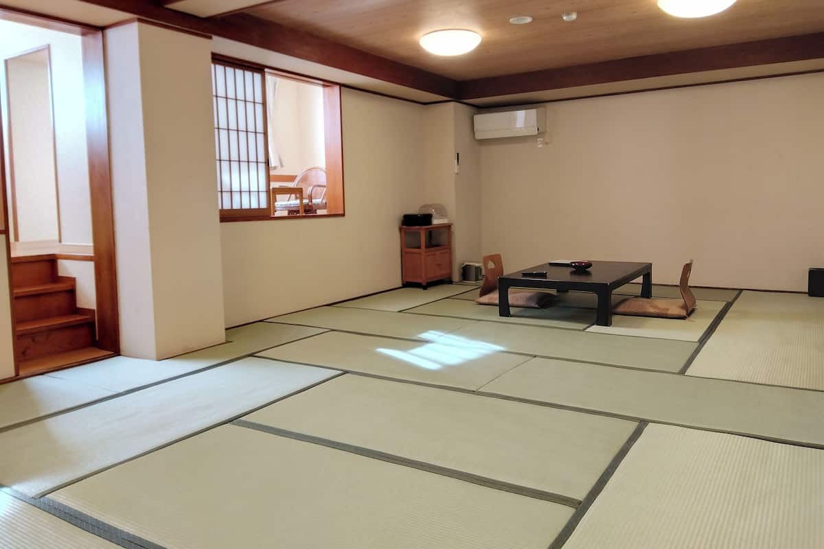 Ein traditioneller japanischer Raum mit Tatami-Bodenbelag, einem niedrigen Tisch mit Kissen, einer Schiebetür und einem Deckenventilator.