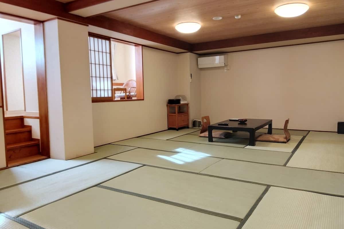 Ein traditioneller japanischer Raum mit Tatami-Bodenbelag, einem niedrigen Tisch mit Kissen, einer Schiebetür und einer Holztreppe.