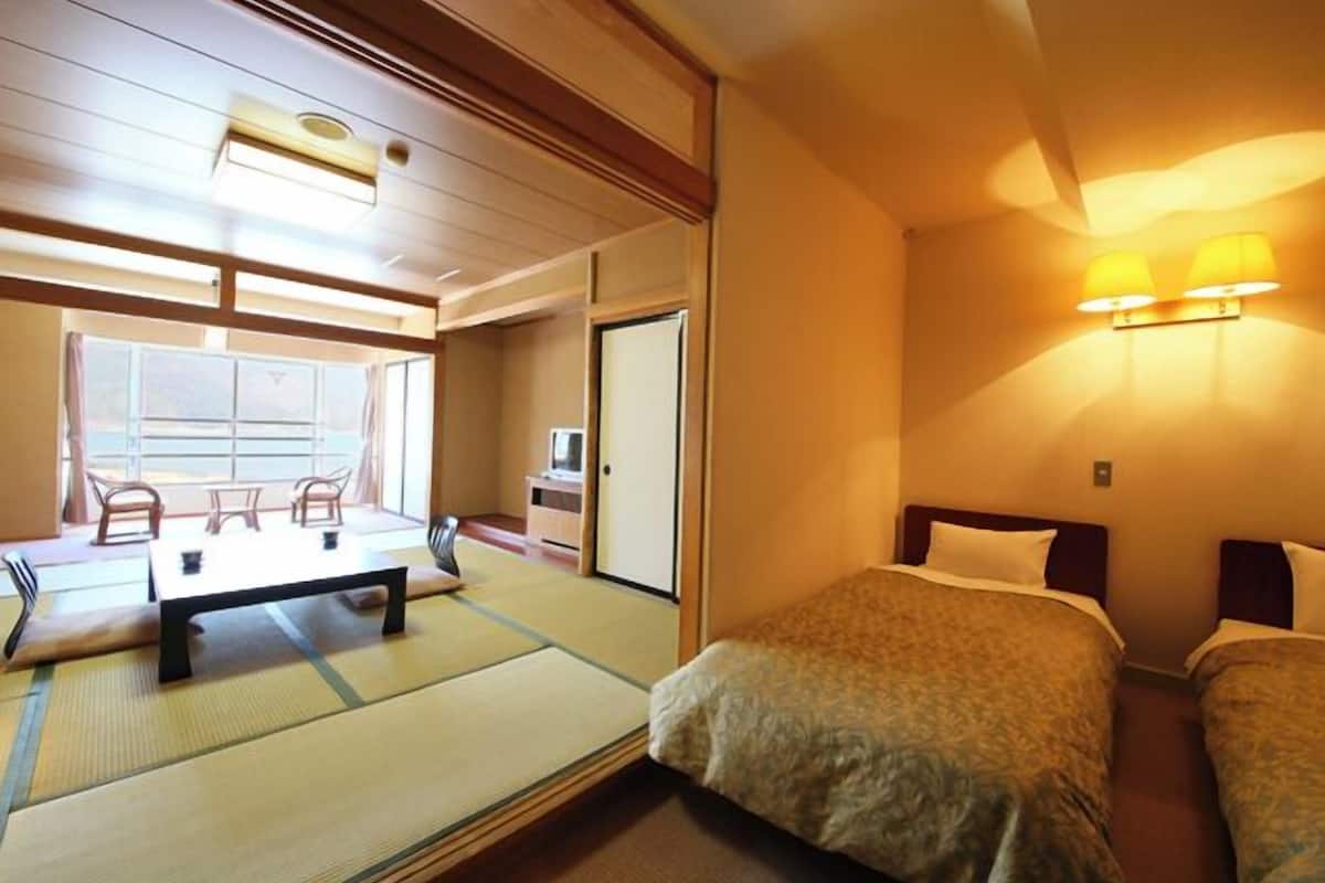 Ein traditionell japanisch eingerichteter Raum mit Tatami-Boden, Futon-Bett, kleinem Schreibtisch mit Stuhl und einer Schiebetür zum Balkon.