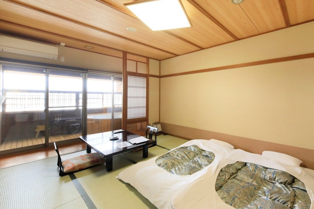 A traditional Japanese room with tatami flooring, a futon bed, a sliding door, and a view of a balcony.