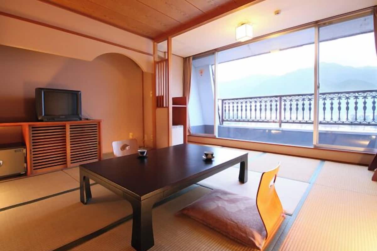 Ein traditioneller japanischer Raum mit Tatami-Böden, einem niedrigen Tisch, einem Fernseher und einem Balkon mit Blick.